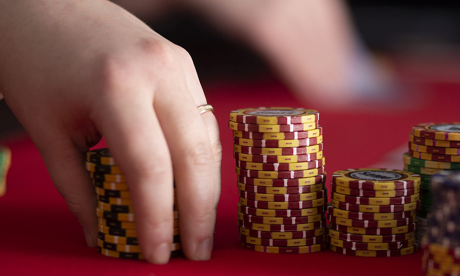 A hand moving stacks of poker chips on a red felt table